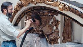 Photographie d'un restaurateur dépoussiérant la surface d'une sculpture à l'aide d'un pinceau à poils souples et d'un aspirateur. Photo CCQ.
