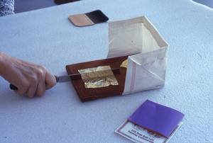On peut voir un petit coussin sur lequel a été déposée un couteau et une feuille d'or. Étant donné la fragilité du matériau, cette façon permet de la diviser sans la briser.