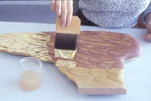 À l'aide d'un pinceau fin et large, le restaurateur applique la feuille d'or.