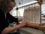 L'image représente une restauratrice de l'atelier des œuvres sur papier procédant à l'assemblage des cahiers avec des fils de lin.