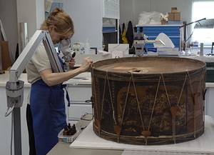 Une restauratrice procède à l'examen du tambour à l'aide de binoculaire.